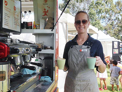young woman working at coffee van holding two reusable mugs with coffee